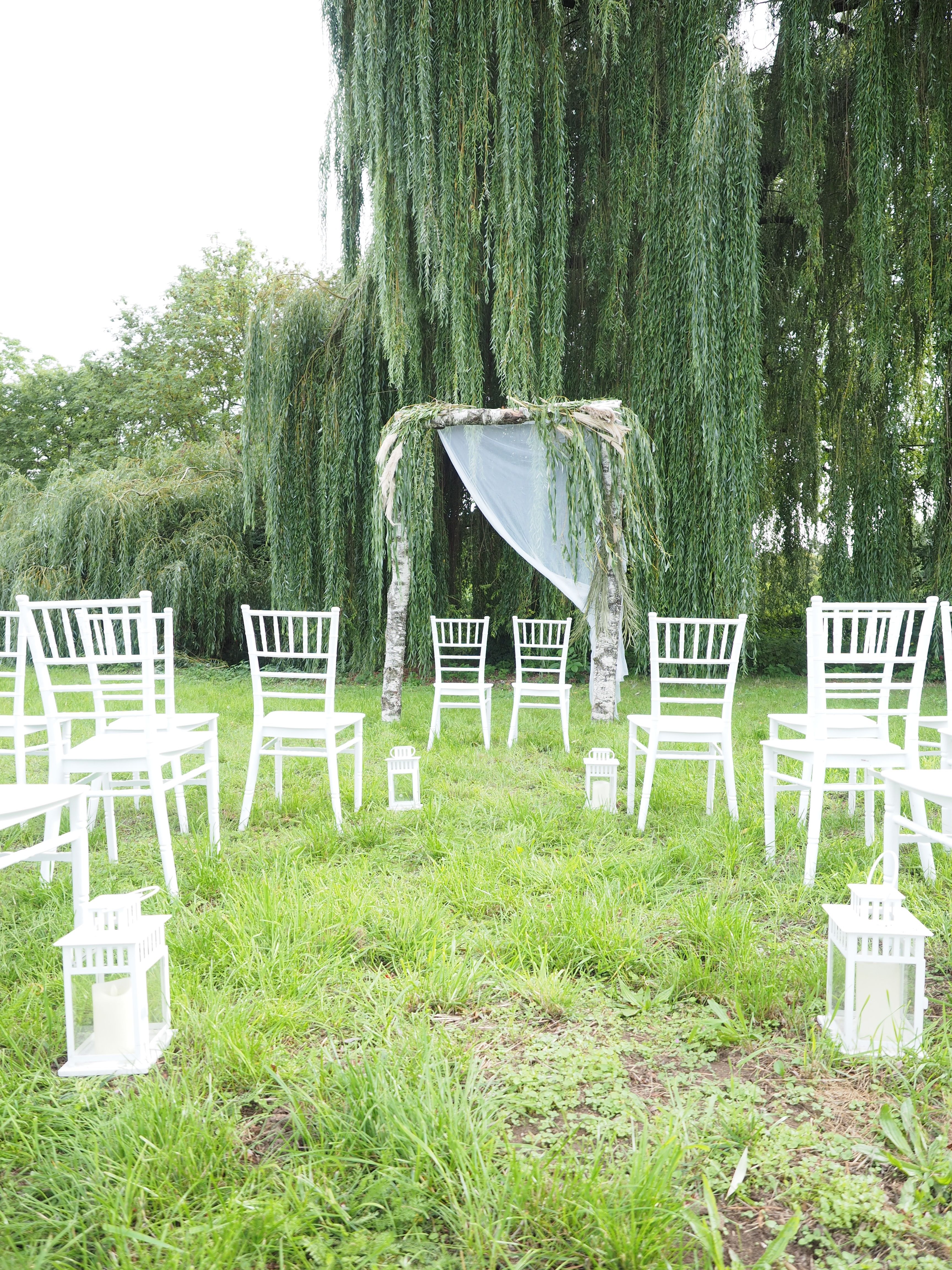 Das Bild zeigt die Möglichkeit einer Außenbestuhlung für z.B. eine Hochzeitsfeier vor einem Birkenholzrahmen, der festlich für eine Trauung geschmückt ist.