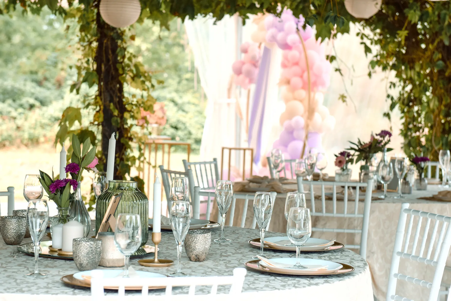 Auf dem Bild ist ein schön dekorierter Tisch zu sehen und im Hintergrund ein großer Bogen mit bunten Luftballons..